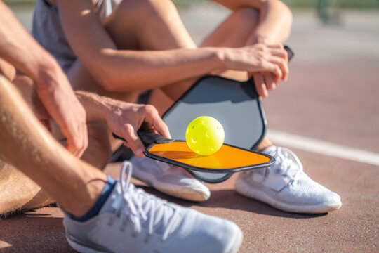  pickleball game, relaxing pickleball players couple with yellow ball with paddle sitting after game, outdoor sport leisure activity.