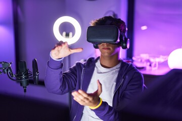 Young hispanic teenager streamer playing video game using virtual reality glasses at gaming room