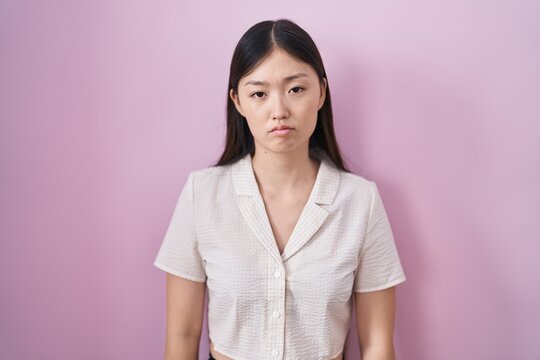 Chinese young woman standing over pink background looking sleepy and tired, exhausted for fatigue and hangover, lazy eyes in the morning.