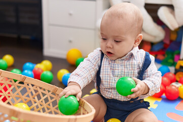 Fototapeta na wymiar Adorable caucasian baby playing with balls sitting on floor at kindergarten
