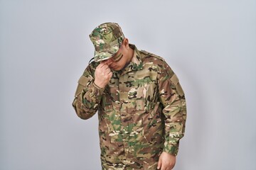 Hispanic young man wearing camouflage army uniform tired rubbing nose and eyes feeling fatigue and headache. stress and frustration concept.
