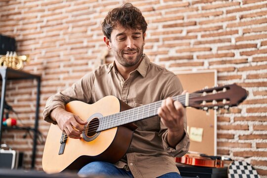 Young man musician smiling confident playing classical guitar at music studio