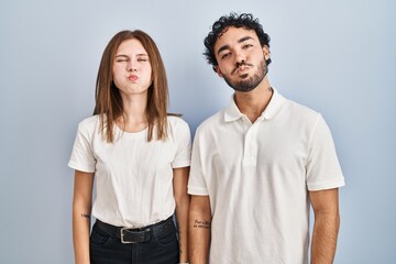 Fototapeta premium Young couple wearing casual clothes standing together puffing cheeks with funny face. mouth inflated with air, crazy expression.