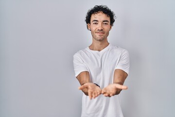 Hispanic man standing over isolated background smiling with hands palms together receiving or giving gesture. hold and protection