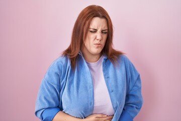 Fototapeta premium Young hispanic woman with red hair standing over pink background with hand on stomach because indigestion, painful illness feeling unwell. ache concept.