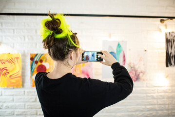 a young woman artist photographs pictures on the wall of the gallery. 