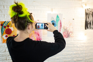 a young woman artist photographs pictures on the wall of the gallery.