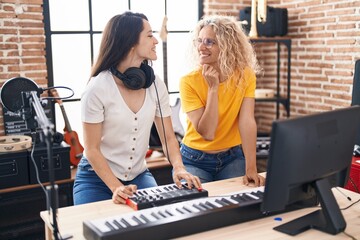 Two women musicians composing song using keyboard at music studio