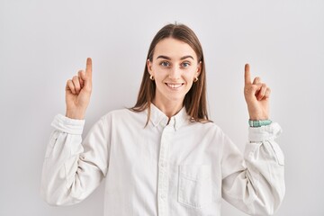 Young caucasian woman standing over isolated background smiling amazed and surprised and pointing up with fingers and raised arms.