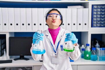 Young asian woman working at scientist laboratory looking at the camera blowing a kiss being lovely and sexy. love expression.