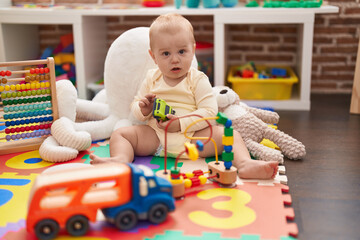 Adorable caucasian baby holding hoop toy sitting on floor at kindergarten