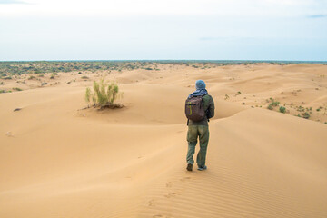 One man stands on a sand dune in the Kyzylkum desert at sunrise.