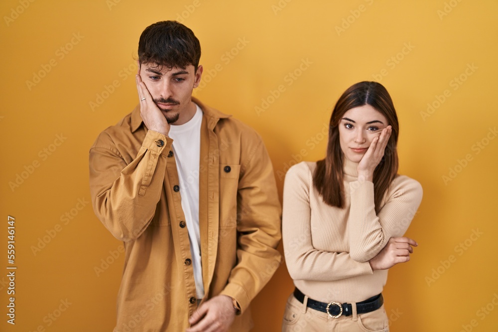 Sticker young hispanic couple standing over yellow background thinking looking tired and bored with depressi