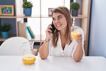Young woman talking on smartphone drinking orange juice at home