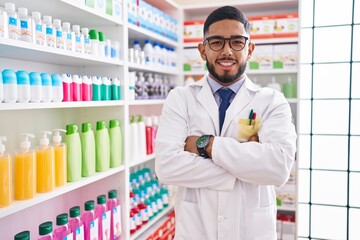 Young latin man pharmacist smiling confident standing with arms crossed gesture at pharmacy