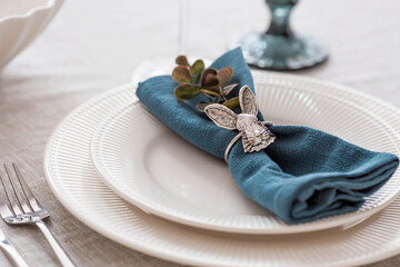 Beautiful spring table setting. A plate with a cotton napkin with a bunny. Silverware and a vase of flowers on a linen tablecloth. The concept of festive serving and a bright Easter holiday.