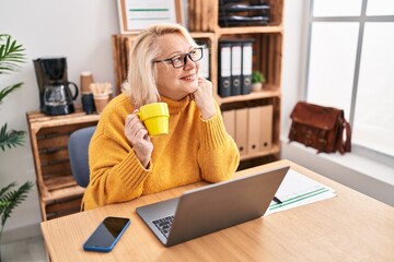 Obraz premium Middle age blonde woman businesswoman drinking coffee working at office