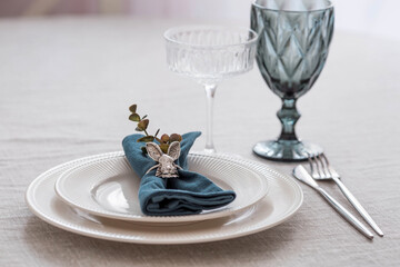 Beautiful spring table setting. A plate with a cotton napkin with a bunny. Silverware and a vase of flowers on a linen tablecloth. The concept of festive serving and a bright Easter holiday.