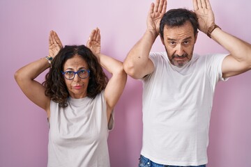 Middle age hispanic couple together over pink background doing bunny ears gesture with hands palms...