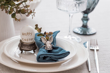 Beautiful spring table setting. A plate with a cotton napkin with a bunny. Silverware and a vase of flowers on a linen tablecloth. The concept of festive serving and a bright Easter holiday.
