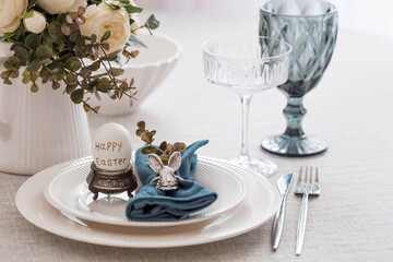 Beautiful spring table setting. A plate with a cotton napkin with a bunny. Silverware and a vase of flowers on a linen tablecloth. The concept of festive serving and a bright Easter holiday.
