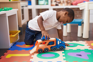 African american boy playing with cars and truck toy sitting on floor at kindergarten