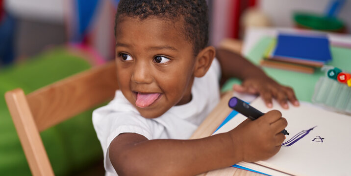 African american boy preschool student sitting on table drawing on notebook at kindergarten