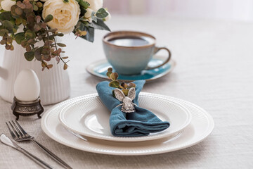 Beautiful spring table setting. A plate with a cotton napkin with a bunny. Silverware and a vase of flowers on a linen tablecloth. The concept of festive serving and a bright Easter holiday.