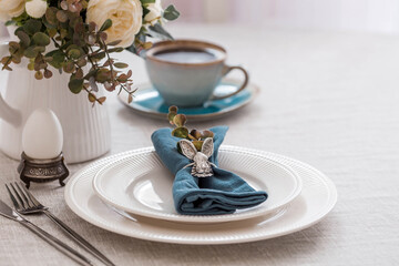 Beautiful spring table setting. A plate with a cotton napkin with a bunny. Silverware and a vase of flowers on a linen tablecloth. The concept of festive serving and a bright Easter holiday.