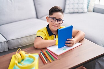 Adorable hispanic boy using touchpad sitting on floor at home