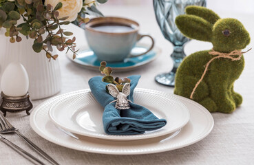 Beautiful spring table setting. A plate with a cotton napkin with a bunny. Silverware and a vase of flowers on a linen tablecloth. The concept of festive serving and a bright Easter holiday.