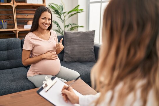 Young pregnant woman at therapy session smiling happy and positive, thumb up doing excellent and approval sign