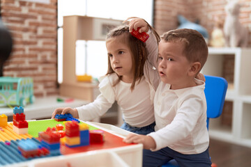 Adorable girl and boy playing with construction block pieces sitting on table at kindergarten