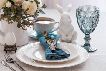 Beautiful spring table setting. A plate with a cotton napkin with a bunny. Silverware and a vase of flowers on a linen tablecloth. The concept of festive serving and a bright Easter holiday.