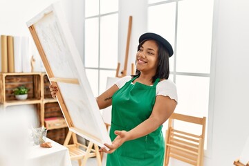 Hispanic brunette woman holding canvas proud of painting at art studio