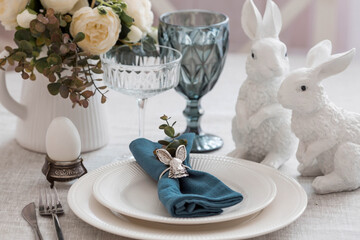 Beautiful spring table setting. A plate with a cotton napkin with a bunny. Silverware and a vase of flowers on a linen tablecloth. The concept of festive serving and a bright Easter holiday.