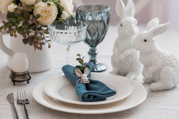 Beautiful spring table setting. A plate with a cotton napkin with a bunny. Silverware and a vase of flowers on a linen tablecloth. The concept of festive serving and a bright Easter holiday.