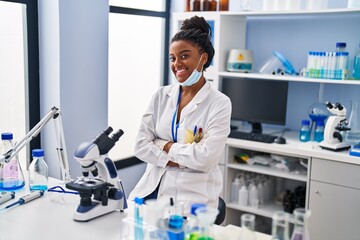 African american woman scientist wearing medical mask with arms crossed gesture at laboratory