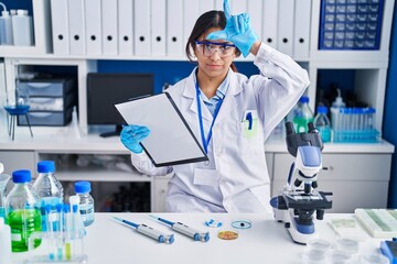Hispanic young woman working at scientist laboratory making fun of people with fingers on forehead doing loser gesture mocking and insulting.