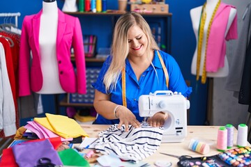 Fototapeta premium Young woman tailor smiling confident using sewing machine at sewing studio