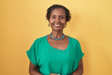 African woman with dreadlocks standing over yellow background with hands together and crossed fingers smiling relaxed and cheerful. success and optimistic