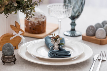 Spring table setting. A plate with a cotton napkin with a bunny, a cake and Easter eggs. Silverware, Easter bunnies and a vase of flowers on a linen tablecloth. The concept of a bright Easter holiday.