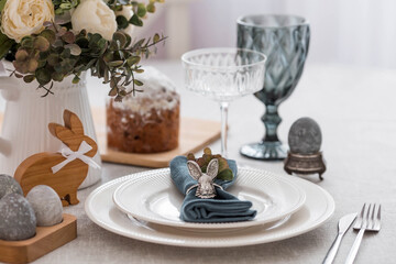 Spring table setting. A plate with a cotton napkin with a bunny, a cake and Easter eggs. Silverware, Easter bunnies and a vase of flowers on a linen tablecloth. The concept of a bright Easter holiday.