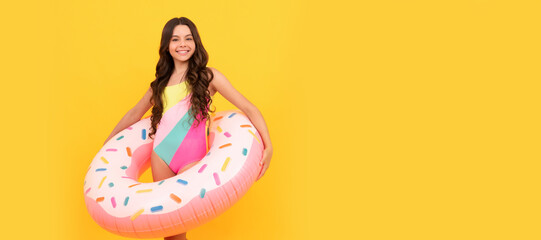 happy teen girl in swimming suit with doughnut inflatable ring on yellow background, summertime. Banner of summer child girl in swimsuit, studio poster header with copy space.