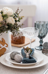 Spring table setting. A plate with a cotton napkin with a bunny, a cake and Easter eggs. Silverware, Easter bunnies and a vase of flowers on a linen tablecloth. The concept of a bright Easter holiday.