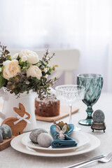 Spring table setting. A plate with a cotton napkin with a bunny, a cake and Easter eggs. Silverware, Easter bunnies and a vase of flowers on a linen tablecloth. The concept of a bright Easter holiday.