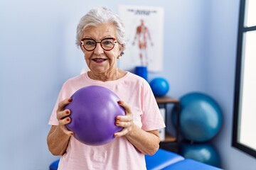 Senior grey-haired woman physitherapist patient having rehab session using ball at physitherapy...