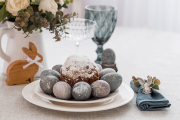 Spring table setting. A plate with a cotton napkin with a bunny, a cake and Easter eggs. Silverware, Easter bunnies and a vase of flowers on a linen tablecloth. The concept of a bright Easter holiday.