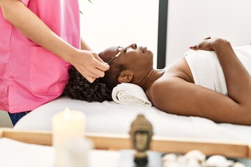 Obraz na płótnie Canvas African american woman lying on massage table having eyebrows treatment at beauty salon
