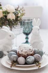 Spring table setting. A plate with a cotton napkin with a bunny, a cake and Easter eggs. Silverware, Easter bunnies and a vase of flowers on a linen tablecloth. The concept of a bright Easter holiday.